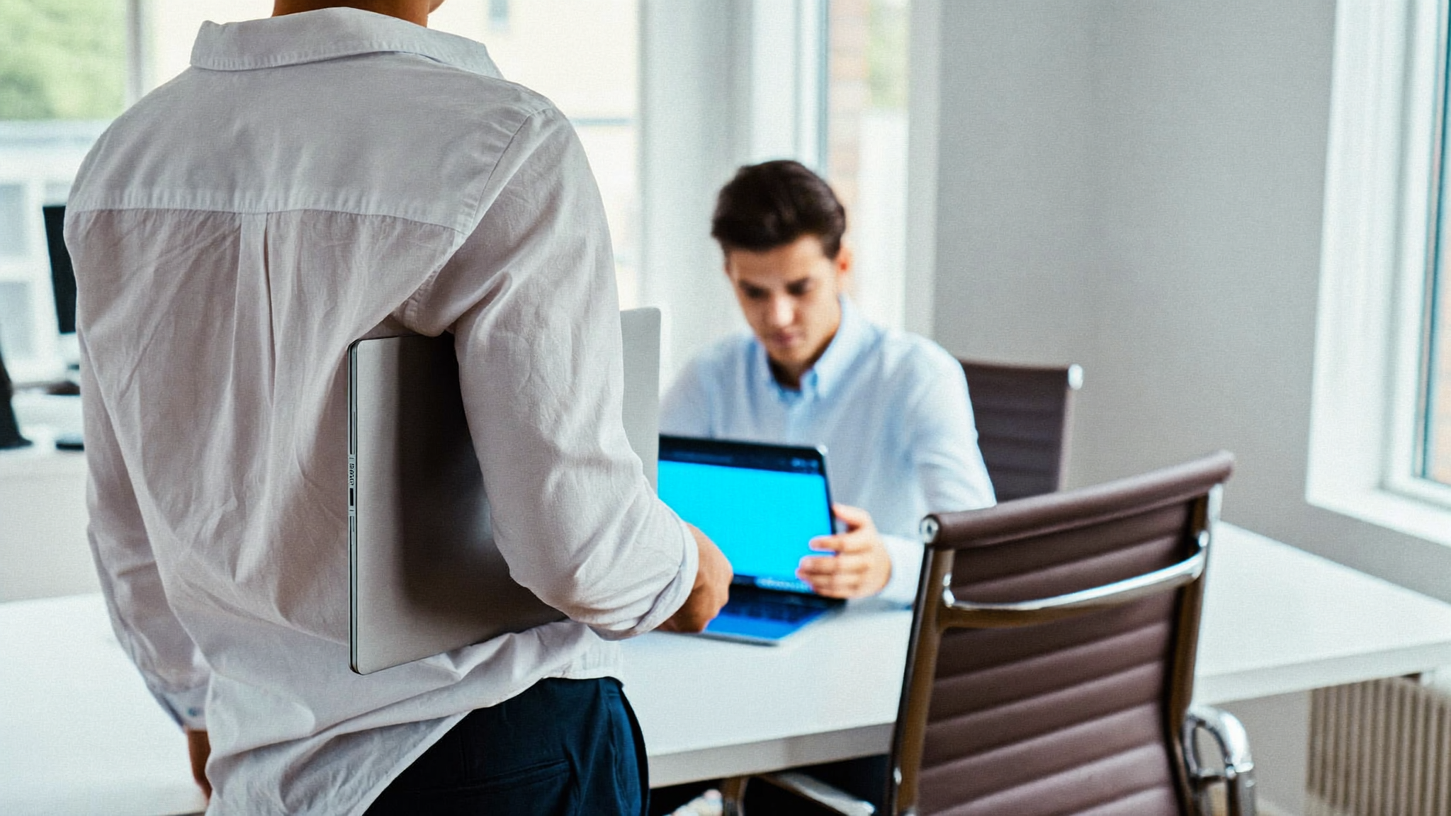 Persona trabajando en su laptop con una interfaz de chat en blanco, escritorio de oficina con luz natural